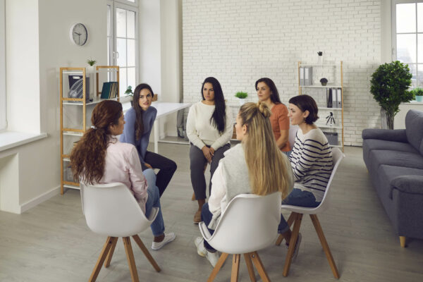 Young women telling their stories in therapy session or support group meeting. Female team talking, sharing news, discussing life situations, giving each other advice, working out solutions together