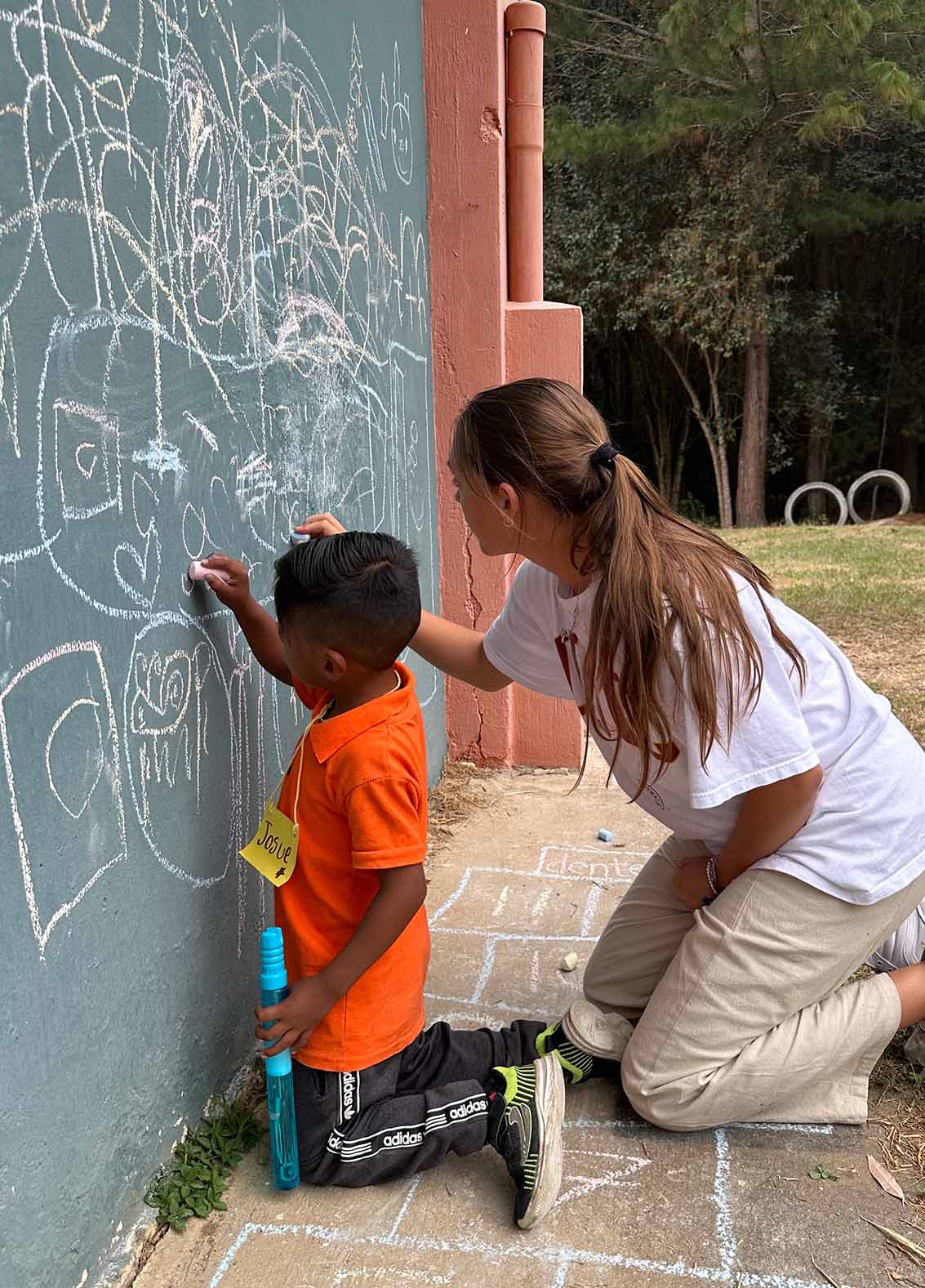 Mission trip participant and boy from Guatemala draw with chalk